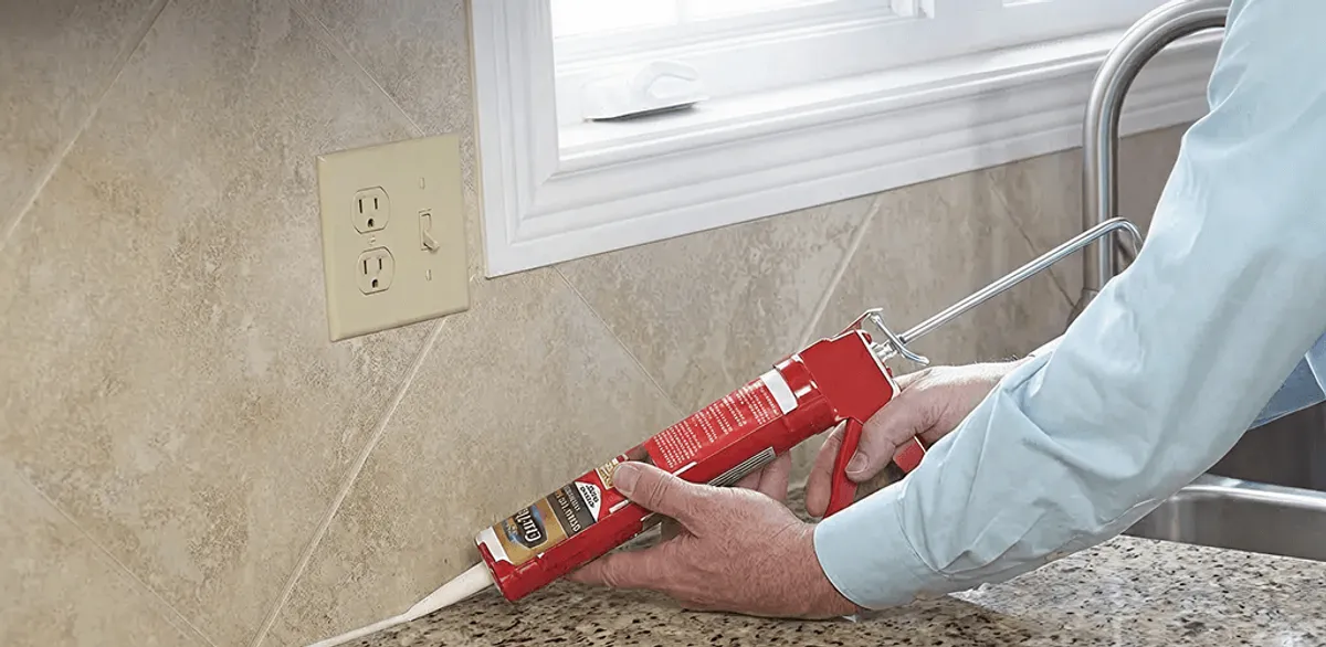 Handyman applying caulk along a kitchen backsplash and countertop seam in Fresno, CA